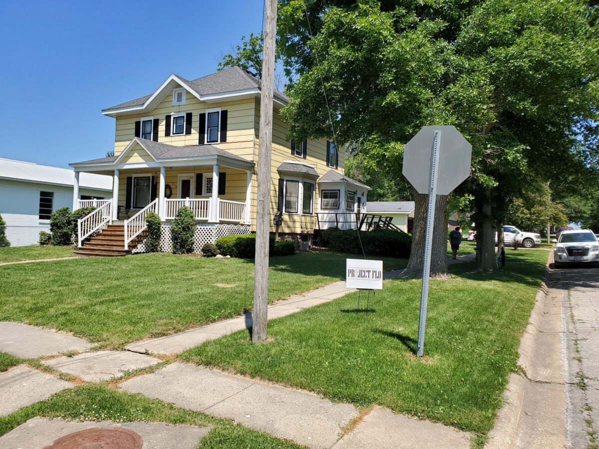 Yellow house with white trim, surrounded by a green lawn. A 