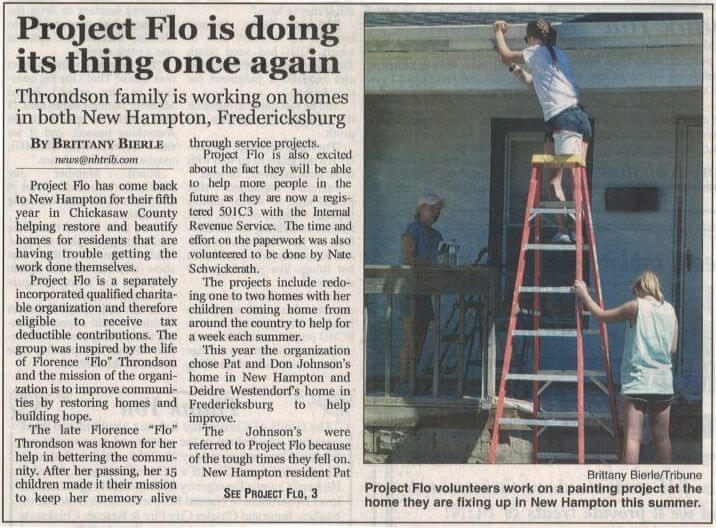 A person on a red ladder paints a part of a house's exterior. The newspaper text details a project working on homes in New Hampton and Fredericksburg.