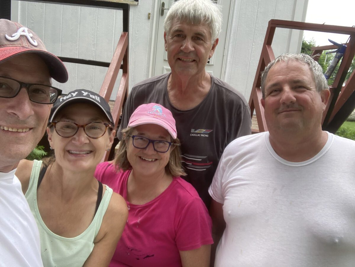 Five people smiling and standing together outdoors in front of steps.